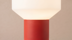Modern light fixture with a red base and white shade on a beige background